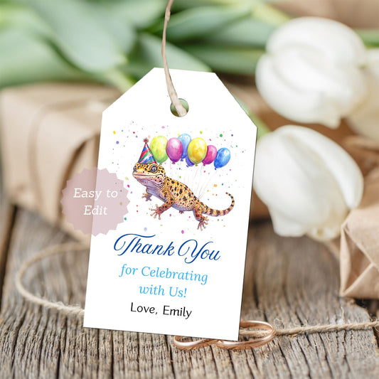 Gift tag with a lizard wearing a party hat and balloons, on a wooden surface with flowers in the background.