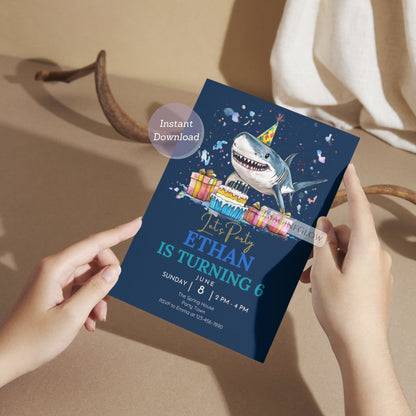 Person holding a shark-themed birthday party invitation card with colorful graphics 