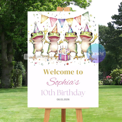 Birthday sign with cartoon frogs wearing party hats and a cake, set outdoors.