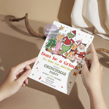 Invitation card for a Grinchmas party held by hands with a neutral background