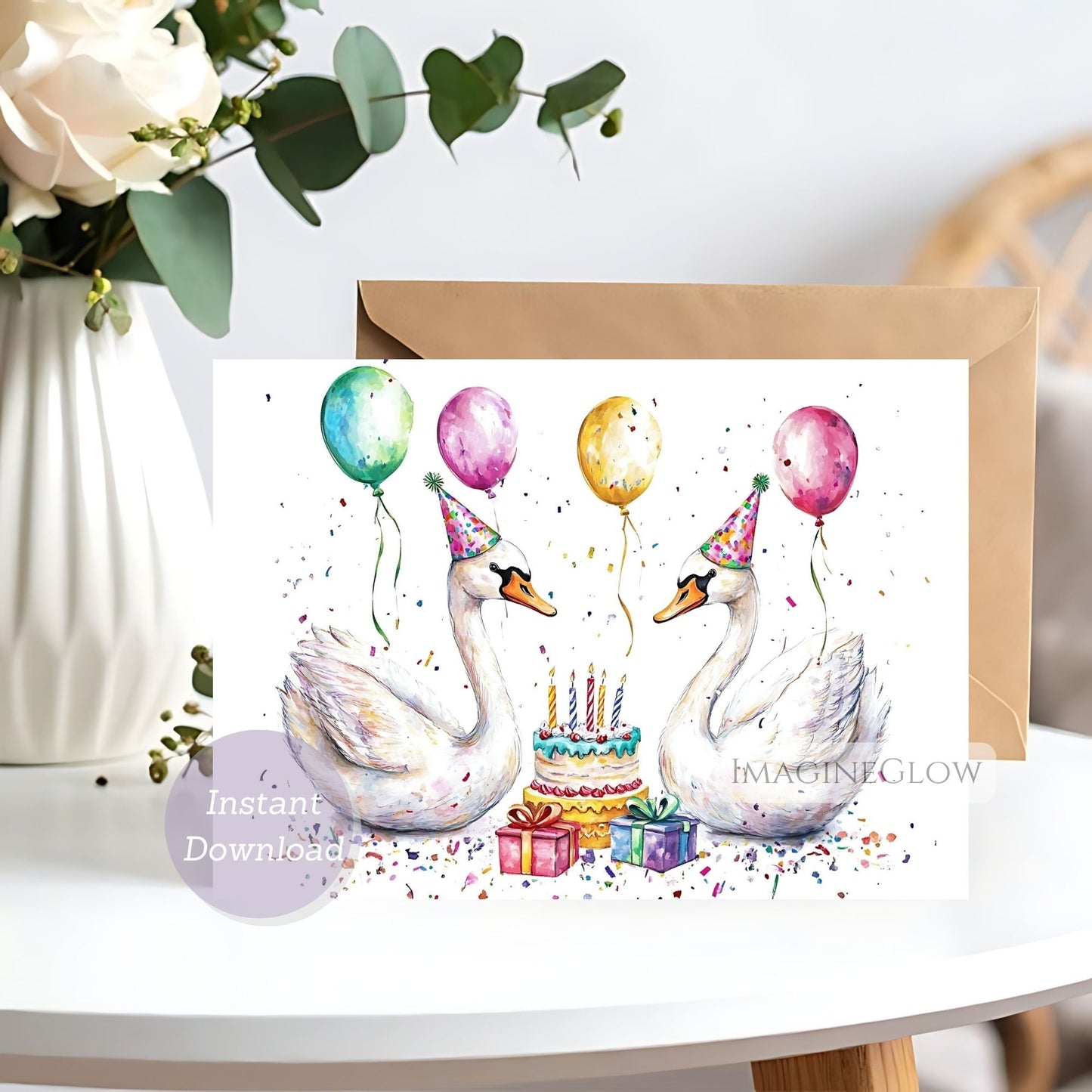 Birthday card with swans, balloons, and a cake on a white surface with flowers in the background.